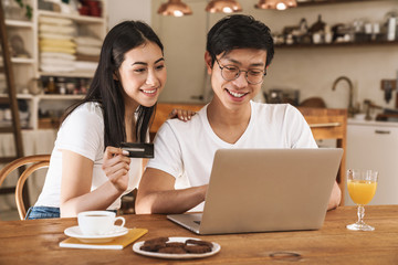 Image of happy couple holding credit card and using laptop