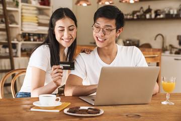 Image of happy couple holding credit card and using laptop