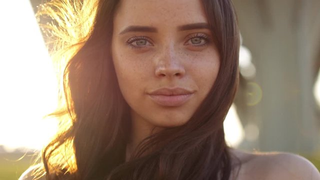 Close-up portrait of beautiful young adult woman in the sunlight at sunset. Pretty girl is smiling. She is cute and funny. Beautiful woman is enjoying warm and sunlight. She is basking in the sun