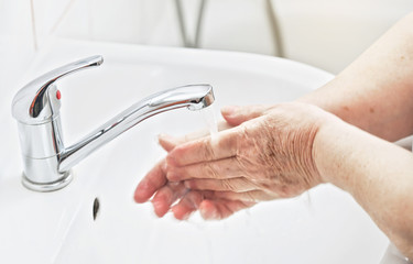 Senior elderly woman wash hands under tap water faucet. Can be used as hygiene illustration concept during coronavirus / covid-19 outbreak prevention
