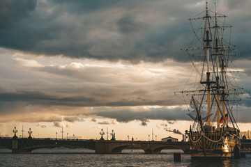 The ship at the embankment in the sunset rays, the dark sea and sky, Vintage frigate on the banks of the Neva. Ship off the coast of St. Petersburg. Flag of Russia is fixed on a vintage frigate.