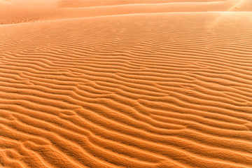 Orange sand lies beautifully in waves at sunset. Sand texture close-up. Hills of yellow sand in Vietnam.