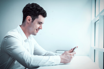 cinematic tone of young Caucasian man using smartphone or cell phone and sitting alone on chair in white room
