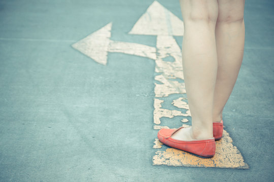 Vintage Tone Of Girl Wear Red Shoes  Walking Towards With Yellow Traffic Arrow Signage On An Asphalt Road