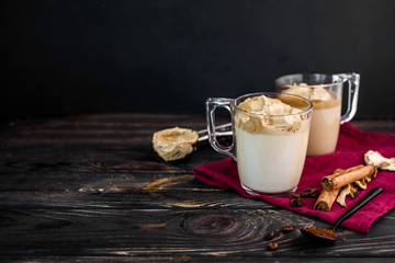 Delicious and fragrant dalgona coffee in glass cups, cinnamon sticks, dried mushrooms, a spoon of instant coffee, sugar.