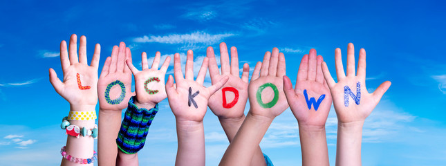 Kids Hands Holding Colorful English Word Lockdown. Blue Sky As Background