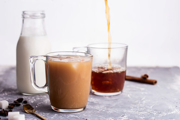 Cooled coffee with milk, cinnamon sticks, coffee beans, sugar, spoon on the table.