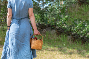 The woman in the blue dress carries a basket with strawberries