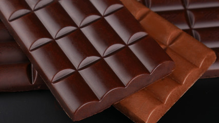 Tiles of black and milk chocolate close-up on a black background with selective focus.