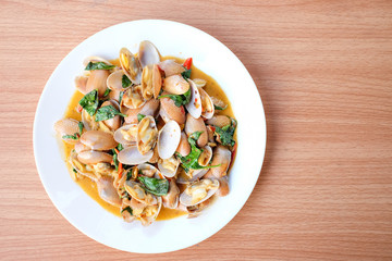 The hot stir fried clams with roasted chili paste and basil serve on white dish set on brown table - homemade food concept.