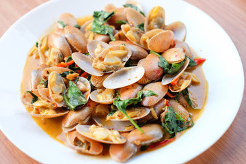 The hot stir fried clams with roasted chili paste and basil serve on white dish set on brown table - homemade food concept.