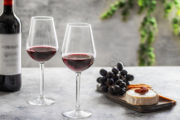 Red wine  bottle with  two glasses and cutting board with different snacks on grey concrete background at restaurant. Wine lover concept
