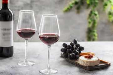 Red wine  bottle with  two glasses and cutting board with different snacks on grey concrete...
