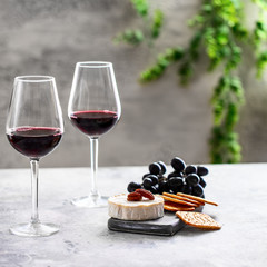 Two red wine glasses and cutting board with dgrapes,cheese and crackers on restaurant table. Wine...