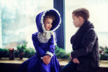Two children, shy boy and girl in vintage retro clothes sitting on window sill together. Girl in vintage violet dress and hat lookink on boy in brown suit with big scarf on neck. Love. Valentine day