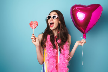 Photo of delighted young woman posing with balloon and lollipop