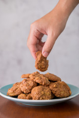 Hand pickup up delicious crunchy homemade chocolate cookies with walnut chunk on top of wooden table and white background. Selective focus on cookies.