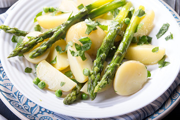 Boiled potato with grilled green asparagus on blue plate over on deep dark background. Overhead.