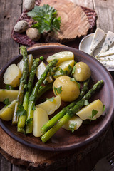 Boiled potato with grilled green asparagus on brown plate over on old wooden background. Overhead. Rustic style.