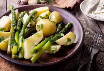 Boiled potato with grilled green asparagus on brown plate over on old wooden background.