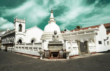 Biała buddyjska świątynia z posągiem Buddy oraz stupą na tle niebieskiego nieba.