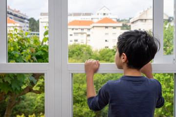 Boy looking out the window of his house waiting for the quarantine to end.