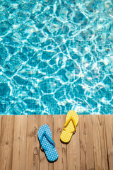 Flip-flops on wooden background near swimming pool