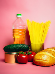 Paper bag with Food supplies crisis food stock for quarantine isolation period on pink. Vermicelli, pasta, canned food, bananas, butter, bread. Food Delivery, Donation, Coronavirus Quarantine.