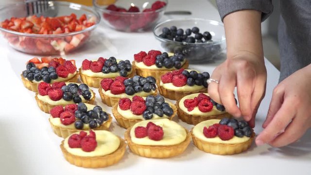 Confectioner decorates tartlets covered with white cream, raspberries, blackberries and strawberries. Confectionery concept