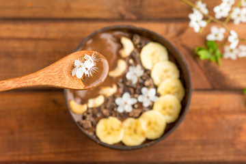 chocolate smoothie with banana and cashew in a coconut bowl and a bamboo spoon