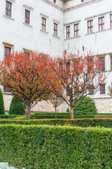 Fototapeta na wymiar Courtyard of a historic castle complex in Trento, Italy. Redleaved autumn Trees mark the way.