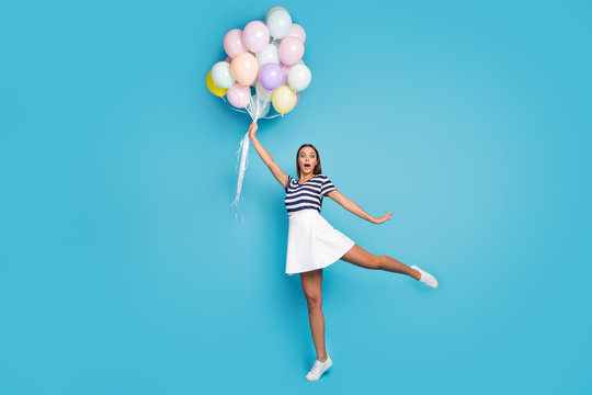 I fly. Full size photo of beautiful funky lady hold many colorful balloons flying up with wind blowing wear striped t-shirt white short skirt shoes isolated blue color background
