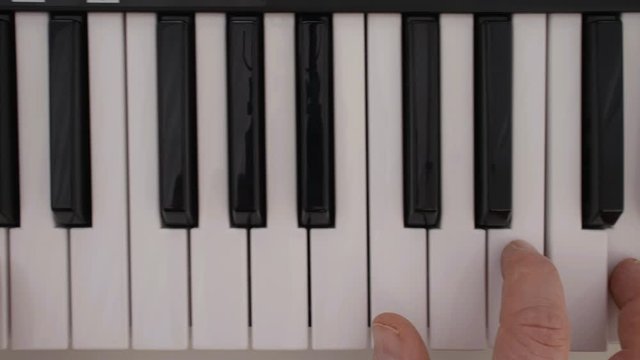 Hands playing electric piano keys. Slow motion close-up as the camera tracks along the keyboard