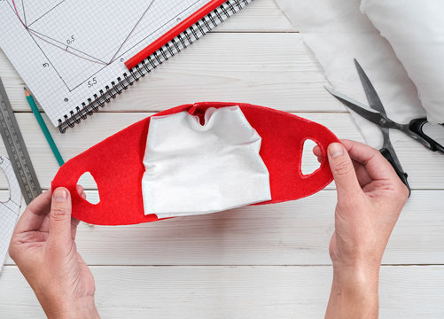 Female hands hold a home-made antiviral mask during isolation and outbreak of the virus. Step-by-step instructions for making a mask yourself. Flat lay, materials for the mask on a white wooden table.