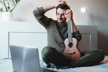 Man sitting at home learns to play ukulele using online lessons.