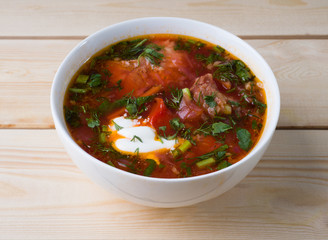 Borsch with sour cream in a white bowl on a wooden background. Side view