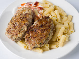 Meat cutlets with a side dish of penne rigate in a white round plate. Close-up