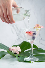 Close up hand, the bartender is mixing soda with strawberries and blueberries in a glass to prepare a cocktail on the green leaves.Food and beverage ideas and copy space.