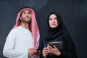 muslim couple using modern technology in front of black chalkboard