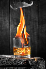 Fire in a whiskey glass with ice on burnt wood