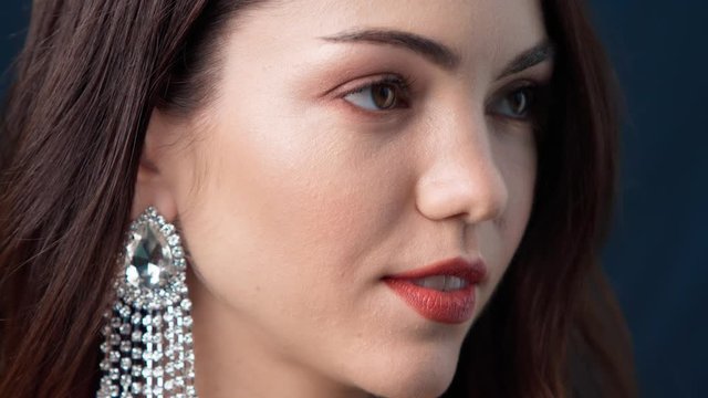 Close-up of the face of a brunette model during a photo shoot. beautiful shiny earrings with stones, bright red lips, make-up, camera flash in the studio