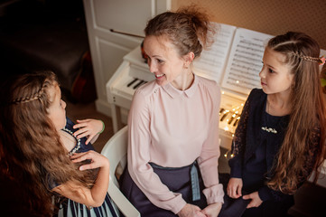 Home piano lesson. A woman and two girls practice sheet music on one musical instrument. Family concept. The idea of activities for children during quarantine.
