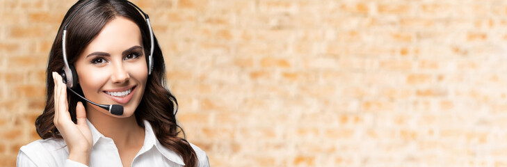 Portrait of happy smiling customer support female phone operator in headset, against loft style wall background. Consulting and assistance service call center.