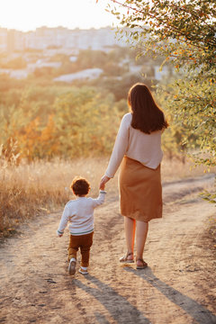 Mom and her little son 2 years old on walk in the autumn park holding hands. Motherhood. Mothers Day. View from back