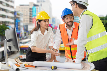 Engineer mixed race caucasian man and asian woman wear hard hat discussing about building plan on computer for construction at job site.