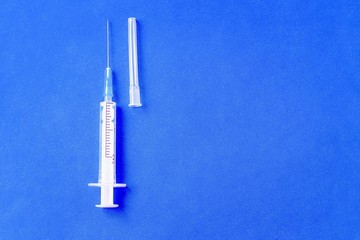 Blank clean injection syringe on blue background. One medical tool. Health care, medicine, medical research, immunization and protection of the population from epidemic or pandemic.