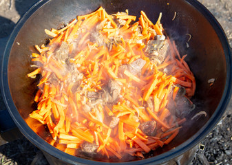 Carrots are fried in oil on a cast-iron cauldron.