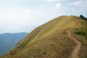 Natural landscape of grassy pathway to the mountain peak with cloudy blue sky