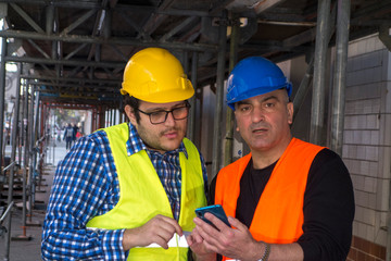 Construction workers at work on construction site using an electronic device. Outdoors