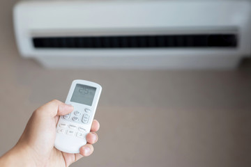 Air conditioner inside the room with close up man hand holding using directed operating remote controller.